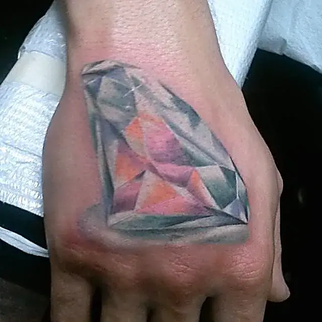 Faceted brilliance: Realistic diamond tattoo on the left hand, rendered in full color.