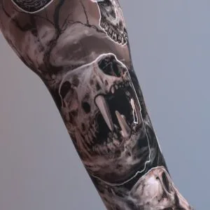 Black and gray sleeve tattoo with multiple skulls including fanged and horned animal skulls